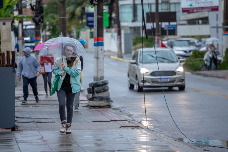 Grande Florianópolis deve enfrentar temporais, foto mostra mulher andando na calçada com guarda-chuva